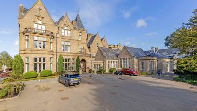 Large stone manor hotel with a parking lot in front containing a grey SUV, a red car, and a golf cart.