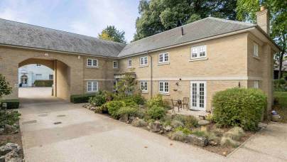 Two-story tan brick building with a stone-paved driveway, a large arched entryway, and a small garden patio.