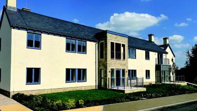 A modern two-story apartment building with white walls, dark-framed windows, and a slate roof.