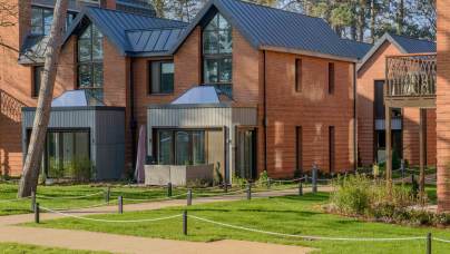 Modern red brick townhouses with metal roofs and grey paneling set behind a grassy lawn with a rope-lined pathway.