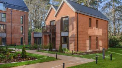 Two modern brick houses with dark metal roofs and balconies, set on a landscaped lot with paved walkways.
