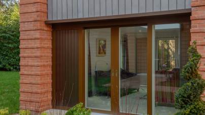 Exterior view of a modern home featuring floor-to-ceiling glass sliding doors framed in brown, flanked by red brick pillars and grey vertical siding.