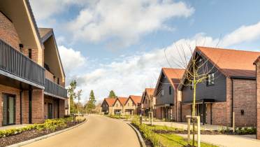 A suburban street with modern brick houses featuring sloped roofs and manicured lawns under a partly cloudy sky.