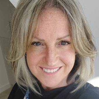 A woman with shoulder-length gray hair smiles at the camera, wearing a dark top with a blue and white pattern.