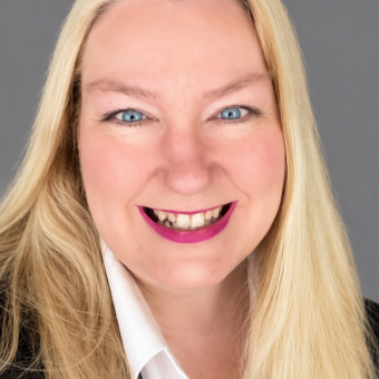 Headshot of a smiling blonde woman wearing a white collared shirt and black blazer.