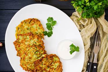 Courgette blini on a white plate served with sour cream and parsley on top