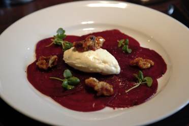 A white plate with beetroot slices, a dollop of cream, candied nuts, and microgreens.
