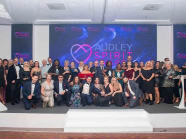 A large group of people in formal attire pose on stage in front of a display that reads "Audley Spirit Awards.