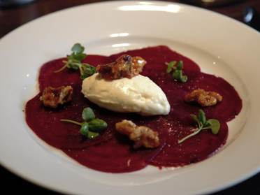 A white plate with beetroot slices, a dollop of cream, candied nuts, and microgreens.