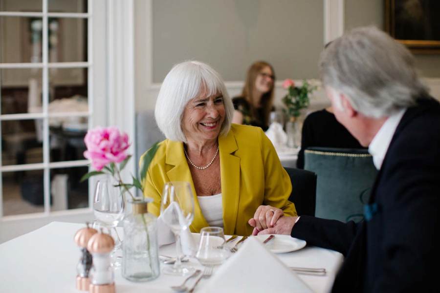 Smiling senior lady in a mustard top sited at a table in restaurant