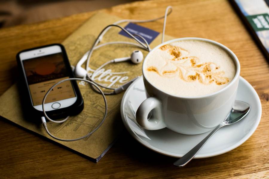 A mobile phone with earphones and a cappuccino on a desk