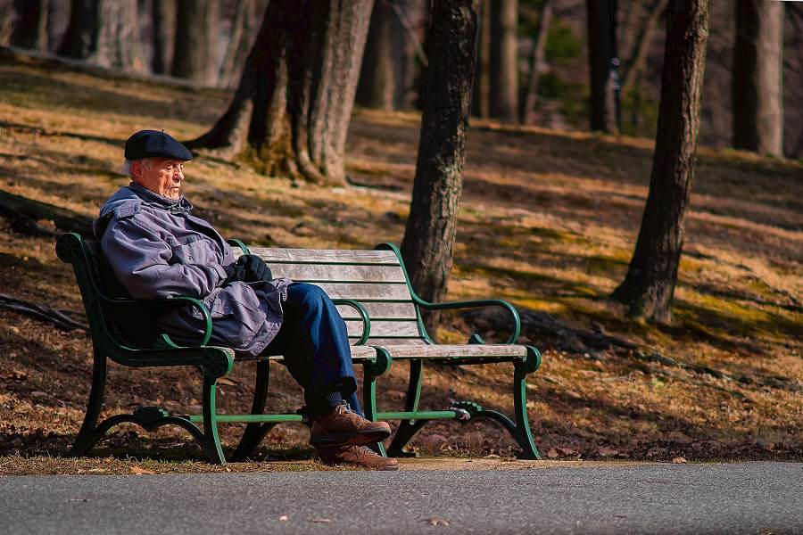 A sad elderly man on a bench in park